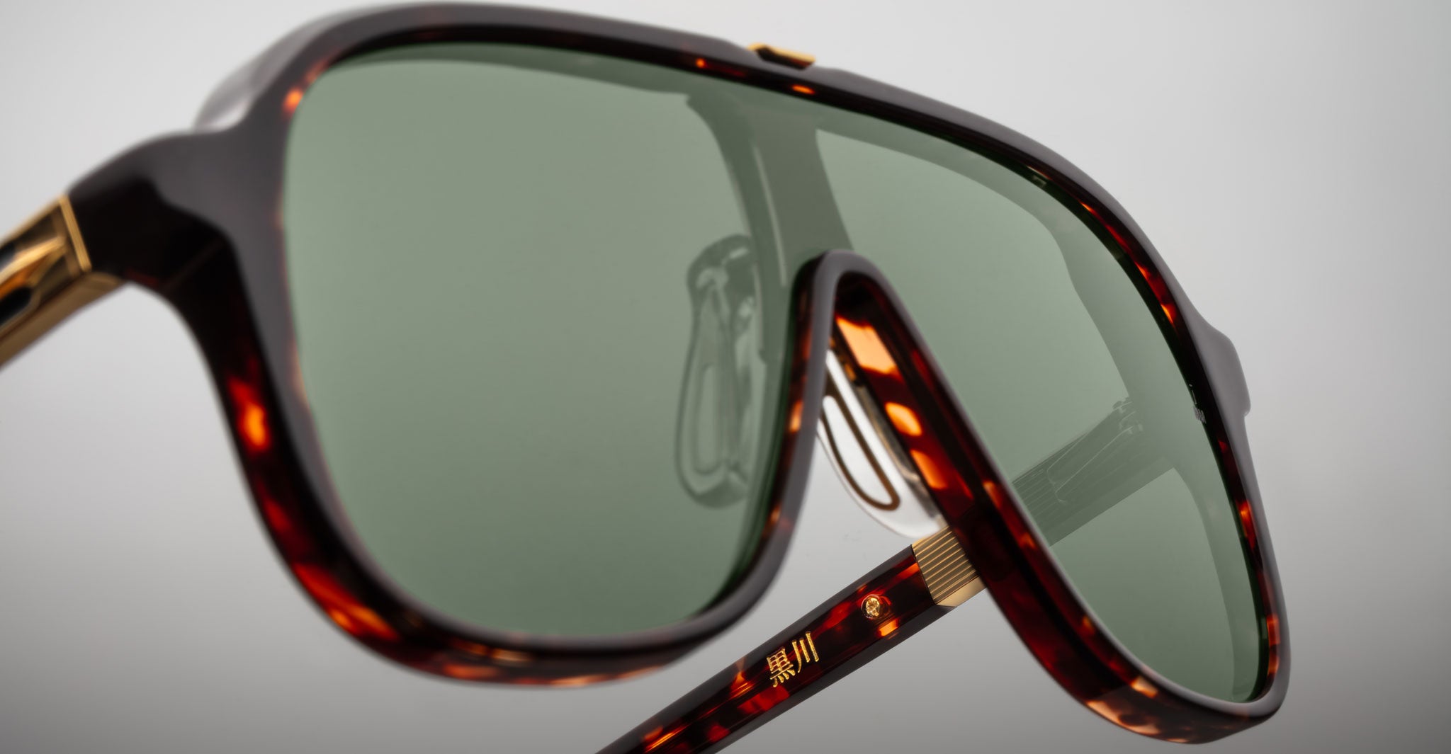 Close-up of Jacques Marie Mage Kurokawa oversized sunglasses featuring green-tinted lenses, a thick tortoiseshell frame, and gold detailing on the arms against a plain light background.