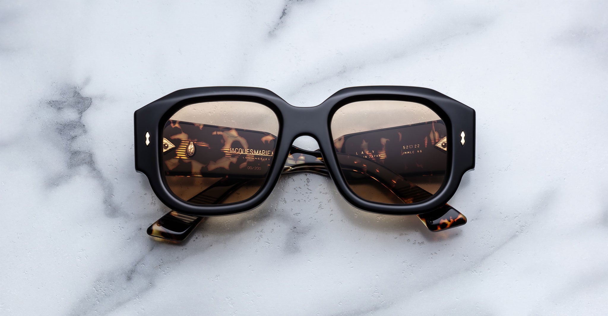 Jacques Marie Mage Lacy square tortoiseshell sunglasses with gold logo, top view showing the frames and branding detail.