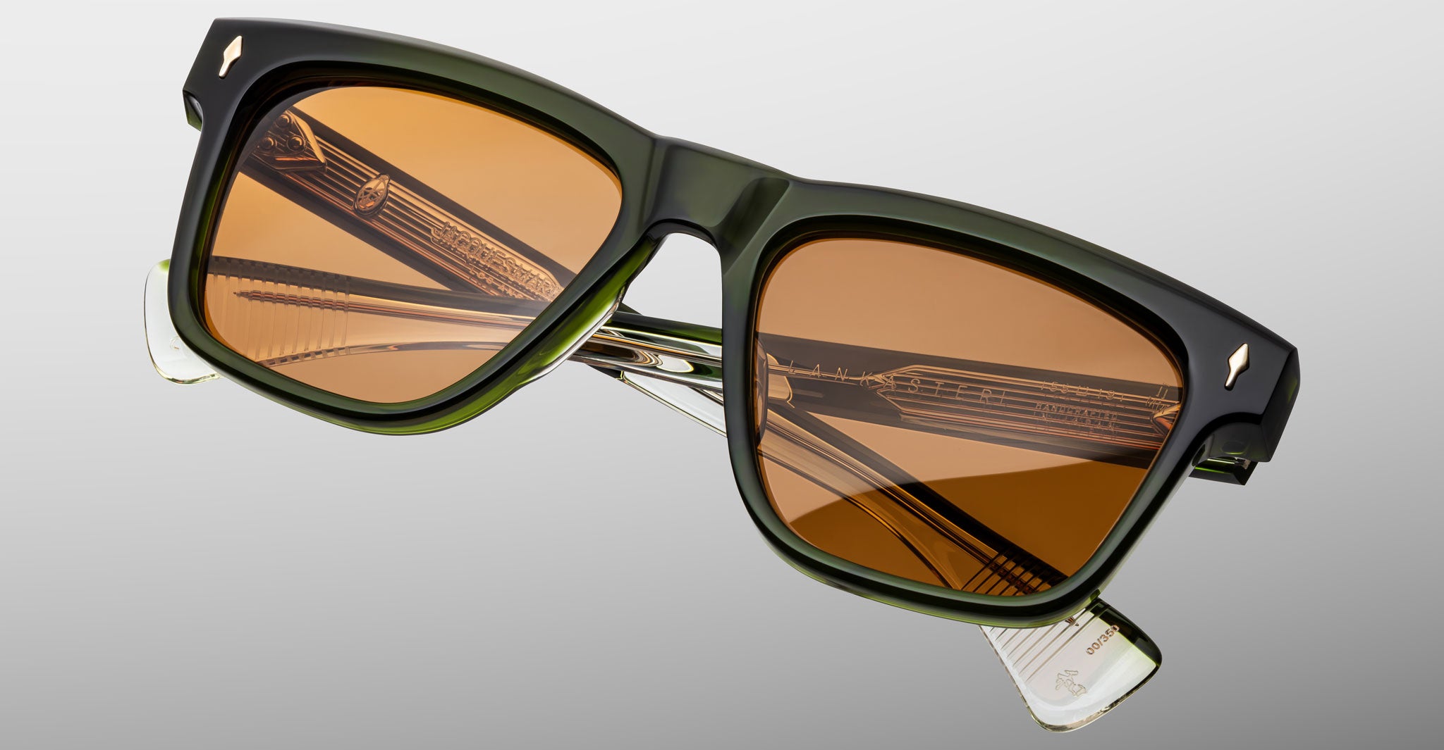 The Jacques Marie Mage Lankaster rectangular sunglasses feature dark green frames, brown-tinted lenses, and metallic inner details on the folded temples, displayed against a gray gradient background.