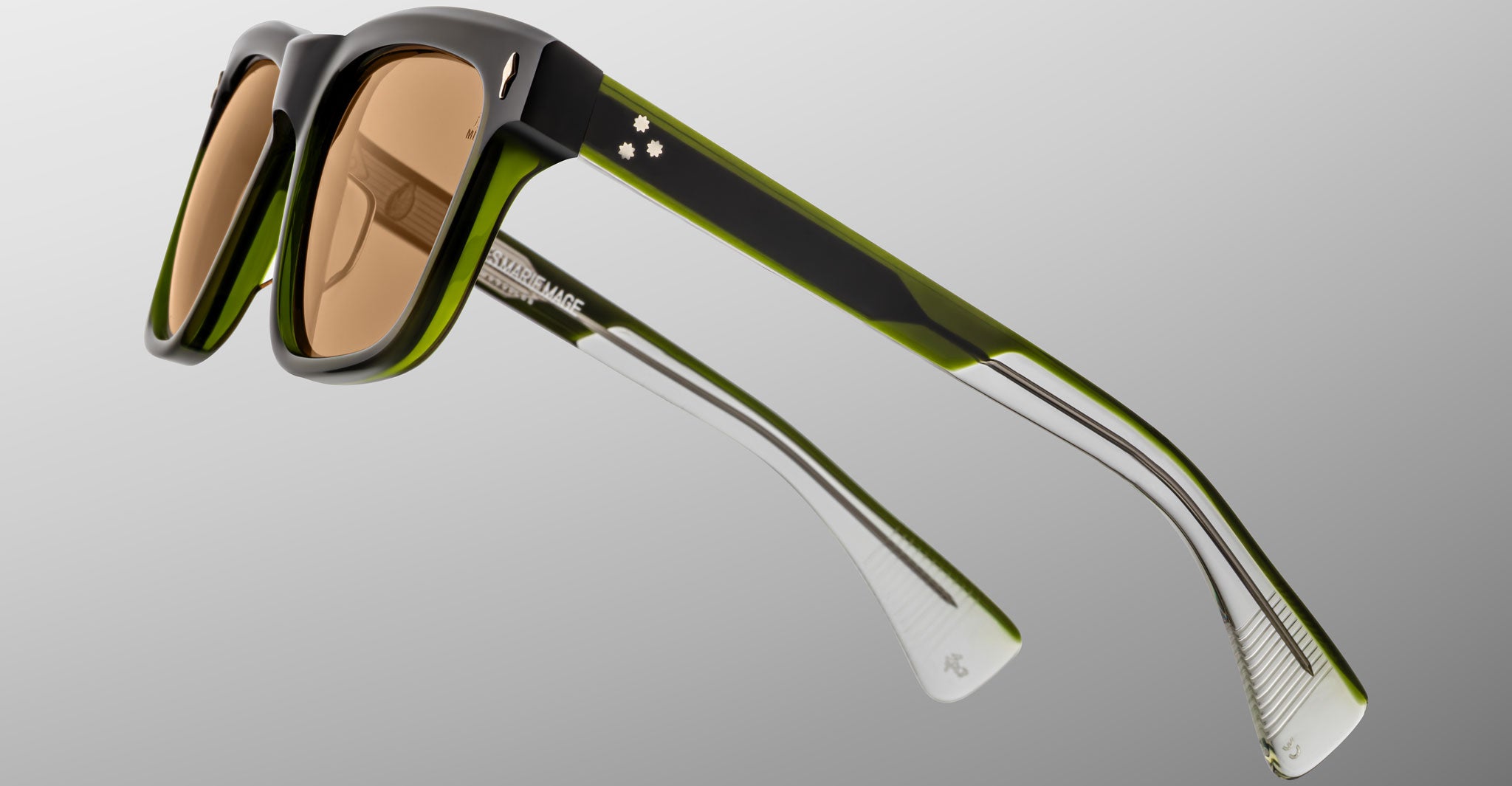 The Jacques Marie Mage Lankaster sunglasses feature thick, square black and green frames, brown-tinted lenses, transparent arm tips, and the brand name visible on the inner side of the arm.