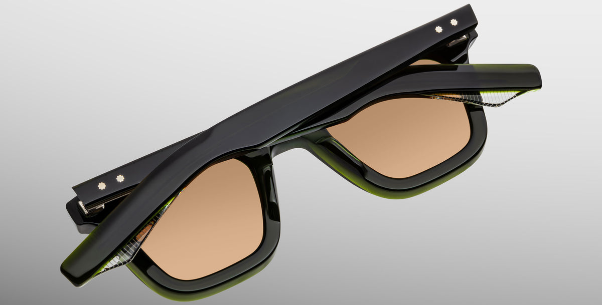 The Jacques Marie Mage Leclair sunglasses, featuring black and green frames with brown-tinted lenses, are displayed folded shut against a plain light gray background.