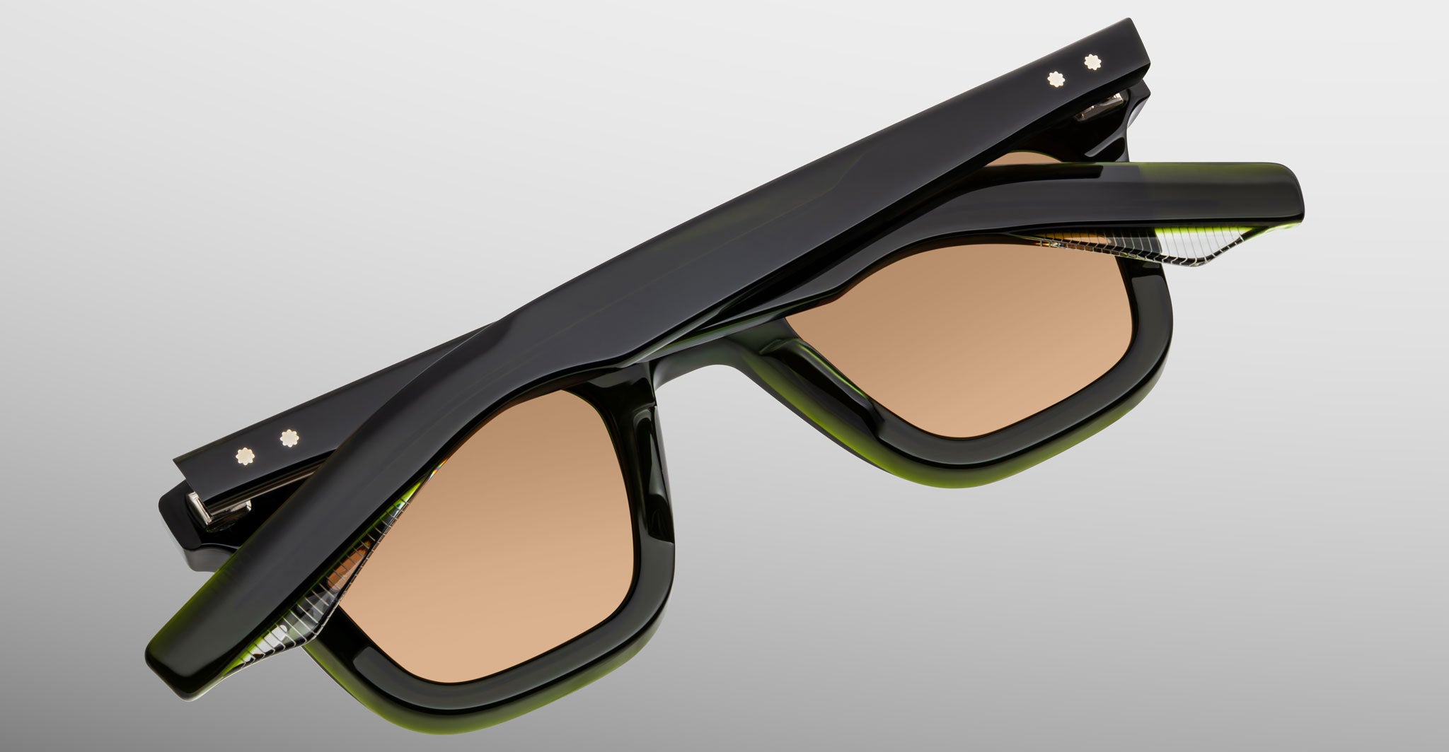 The Jacques Marie Mage Leclair sunglasses, featuring black and green frames with brown-tinted lenses, are displayed folded shut against a plain light gray background.