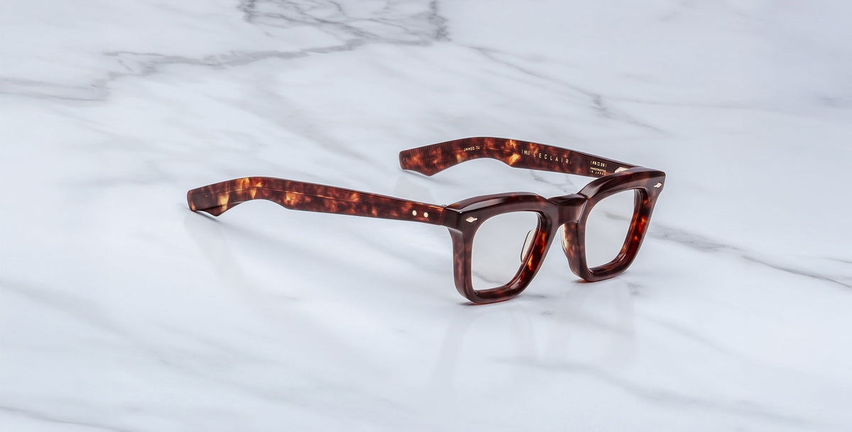 A pair of Jacques Marie Mage Leclair rectangular tortoiseshell eyeglasses with thick frames rests on a white marble surface.