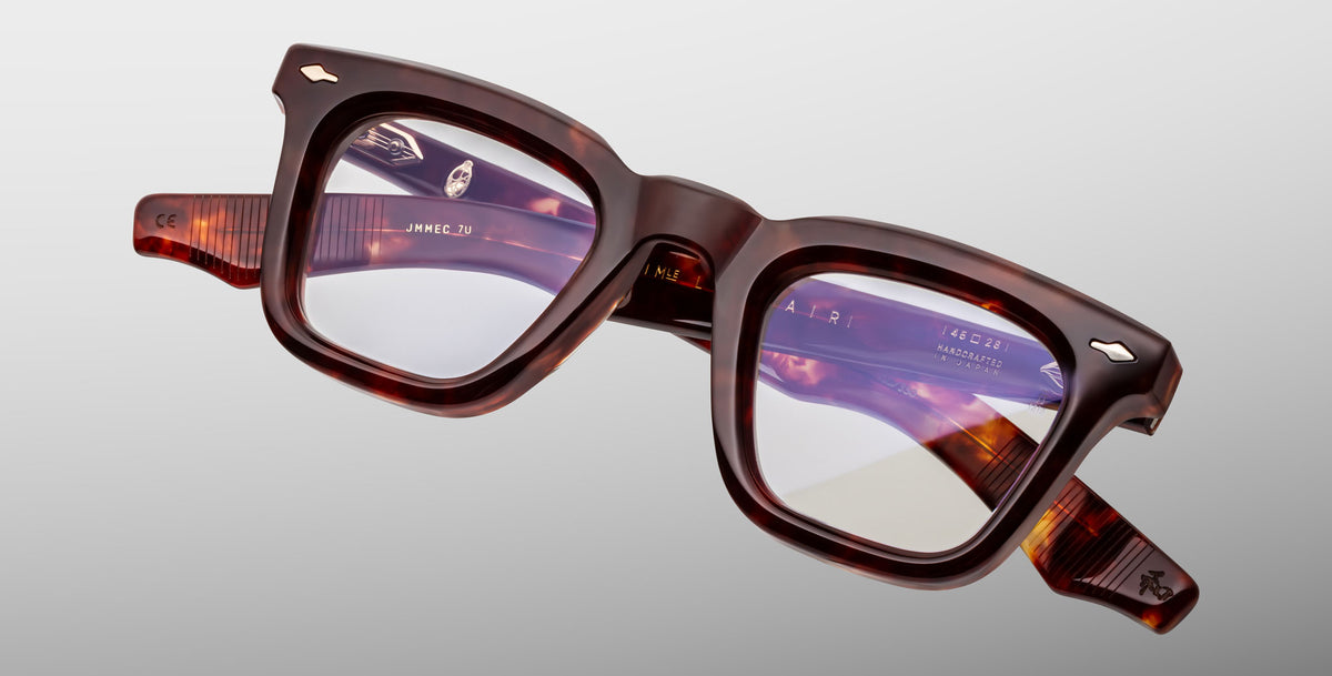 The Jacques Marie Mage Leclair eyeglasses feature thick, square tortoiseshell frames with clear lenses, shown against a plain light gray background. Visible brand markings and details are present on the inner arms.