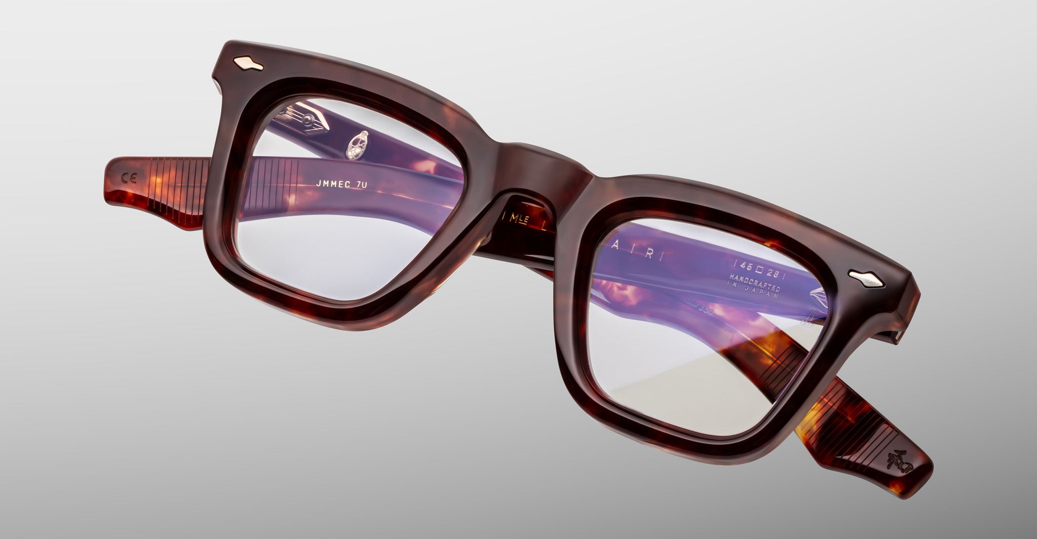 The Jacques Marie Mage Leclair eyeglasses feature thick, square tortoiseshell frames with clear lenses, shown against a plain light gray background. Visible brand markings and details are present on the inner arms.
