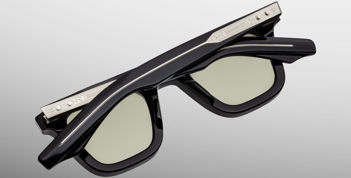 The Jacques Marie Mage Leclair sunglasses, featuring a black rectangular frame with light lenses and silver metal accents engraved on the arms, are shown folded against a neutral background.
