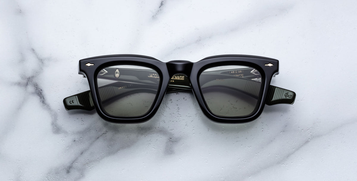 The Jacques Marie Mage Leclair sunglasses, featuring a black rectangular frame with subtle patterned temples and metallic accents near the hinges, rest on a white marble surface. The lenses are dark for a sleek, modern look.