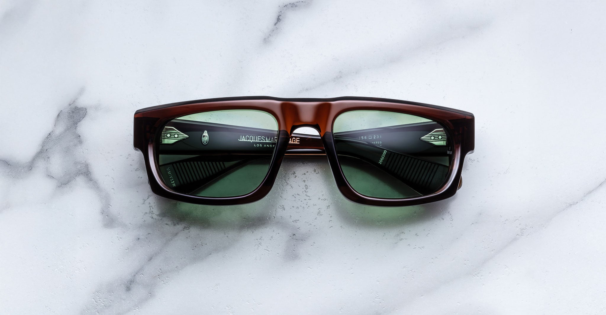 Jacques Marie Mage Louisville sunglasses with brown frames and green lenses, top view, product displayed on a flat surface.