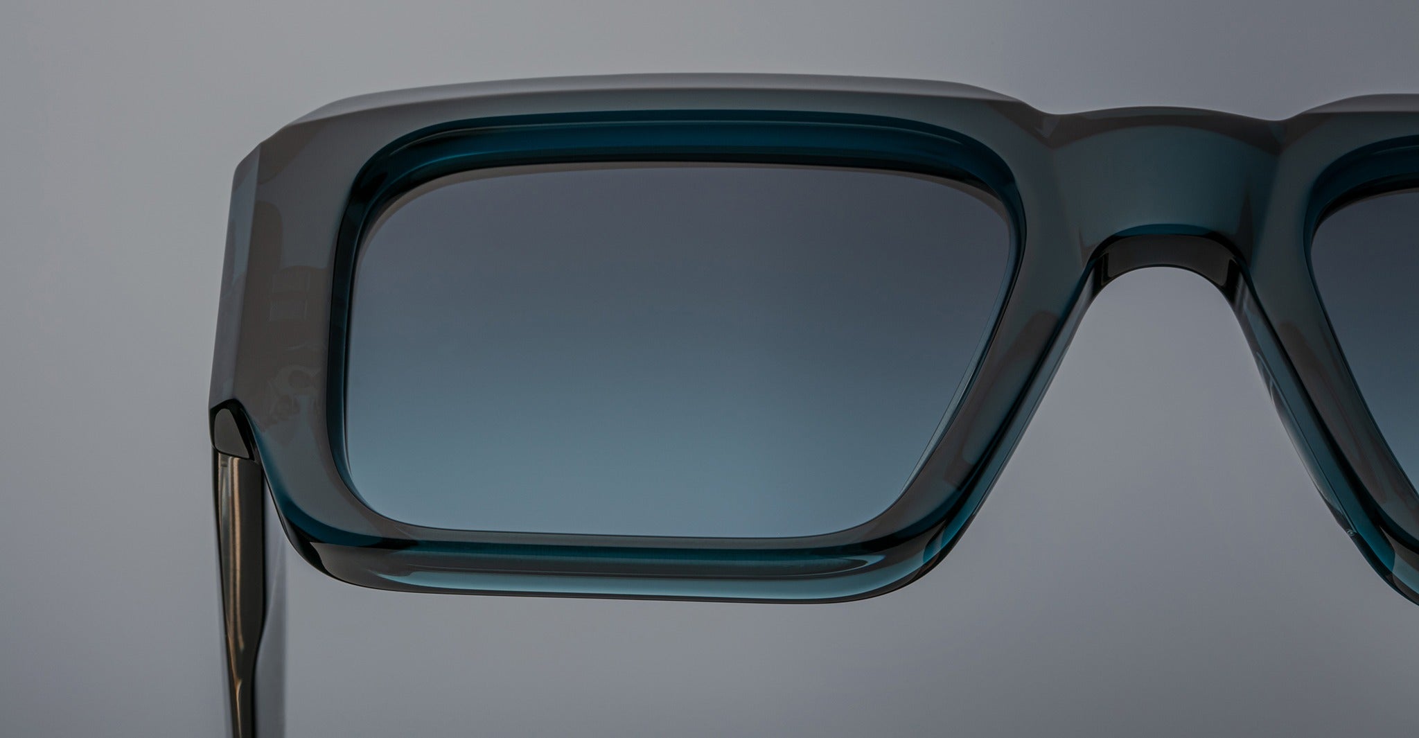 Close-up of the top half of Jacques Marie Mage Miglia rectangular sunglasses in teal with gradient tinted lenses, set against a plain, light gray background.