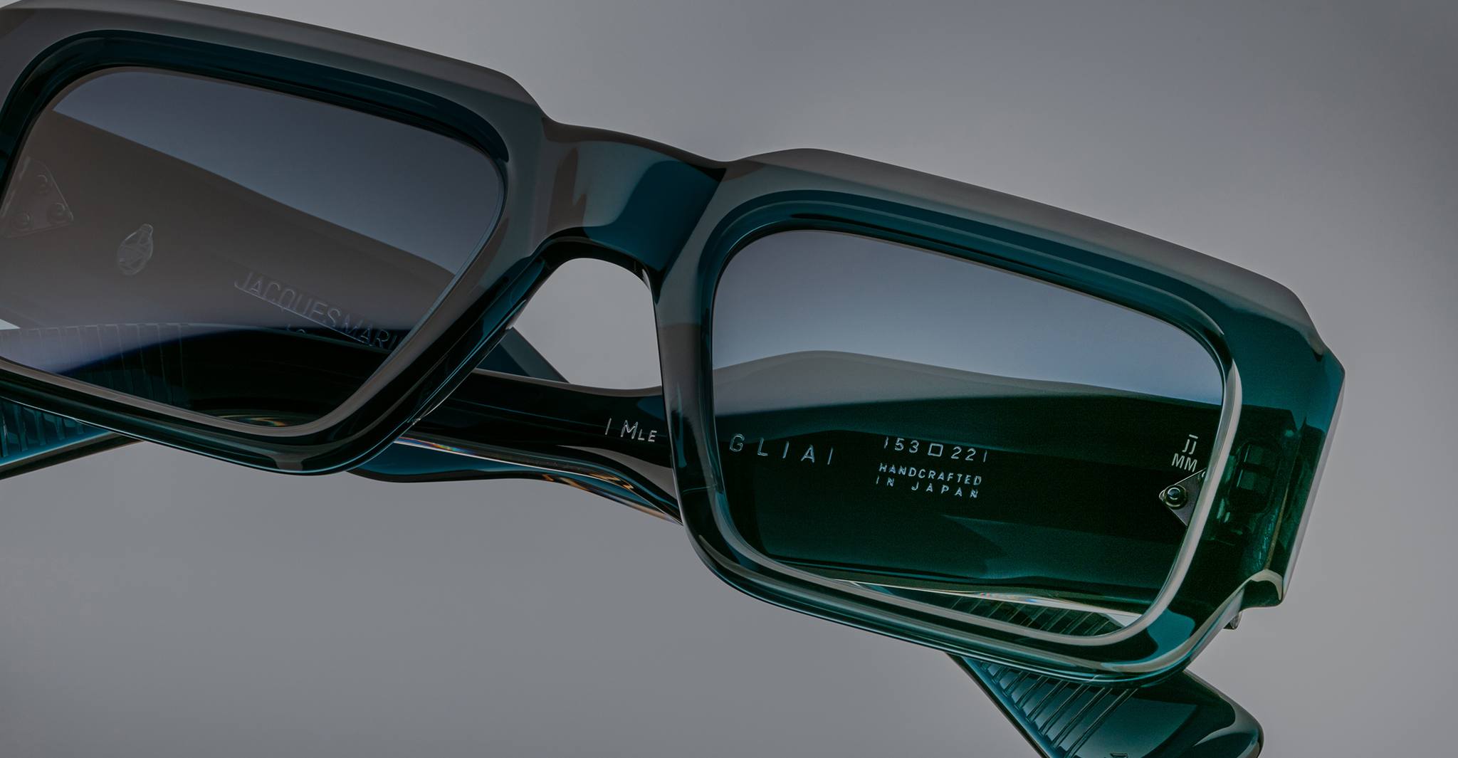 Close-up of Jacques Marie Mage Miglia sunglasses featuring dark green rectangular frames with a thick design, visible brand markings, and lens reflections, set against a neutral background.