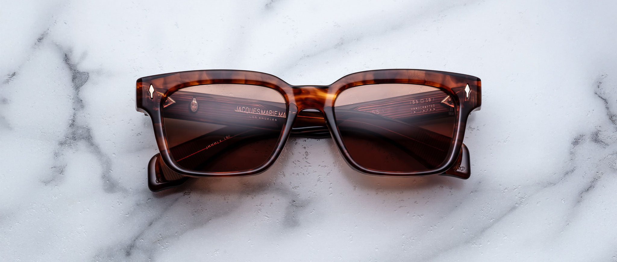 A pair of Jacques Marie Mage Molino 55 brown tortoiseshell square sunglasses with dark lenses rests on a white marble surface.