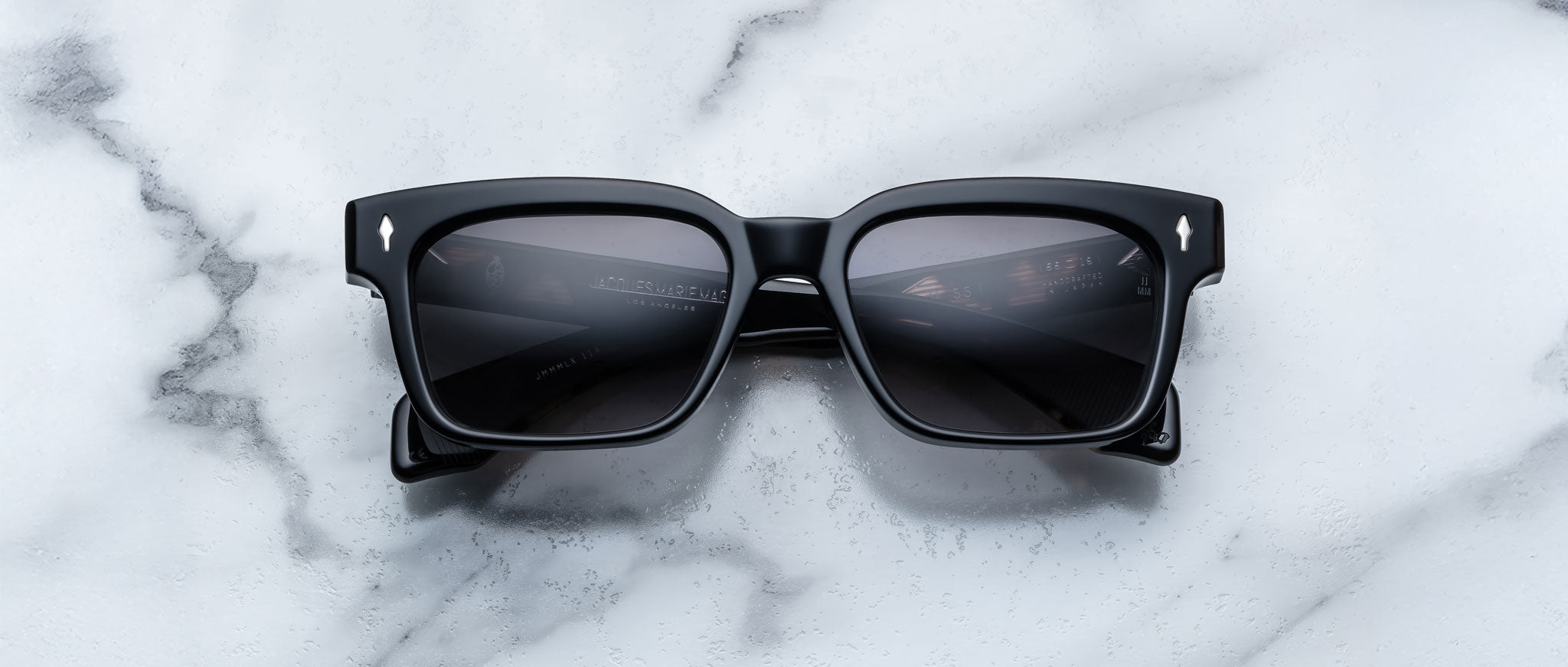 A pair of Jacques Marie Mage Molino 55 black rectangular sunglasses with dark lenses is placed on a white marble surface.