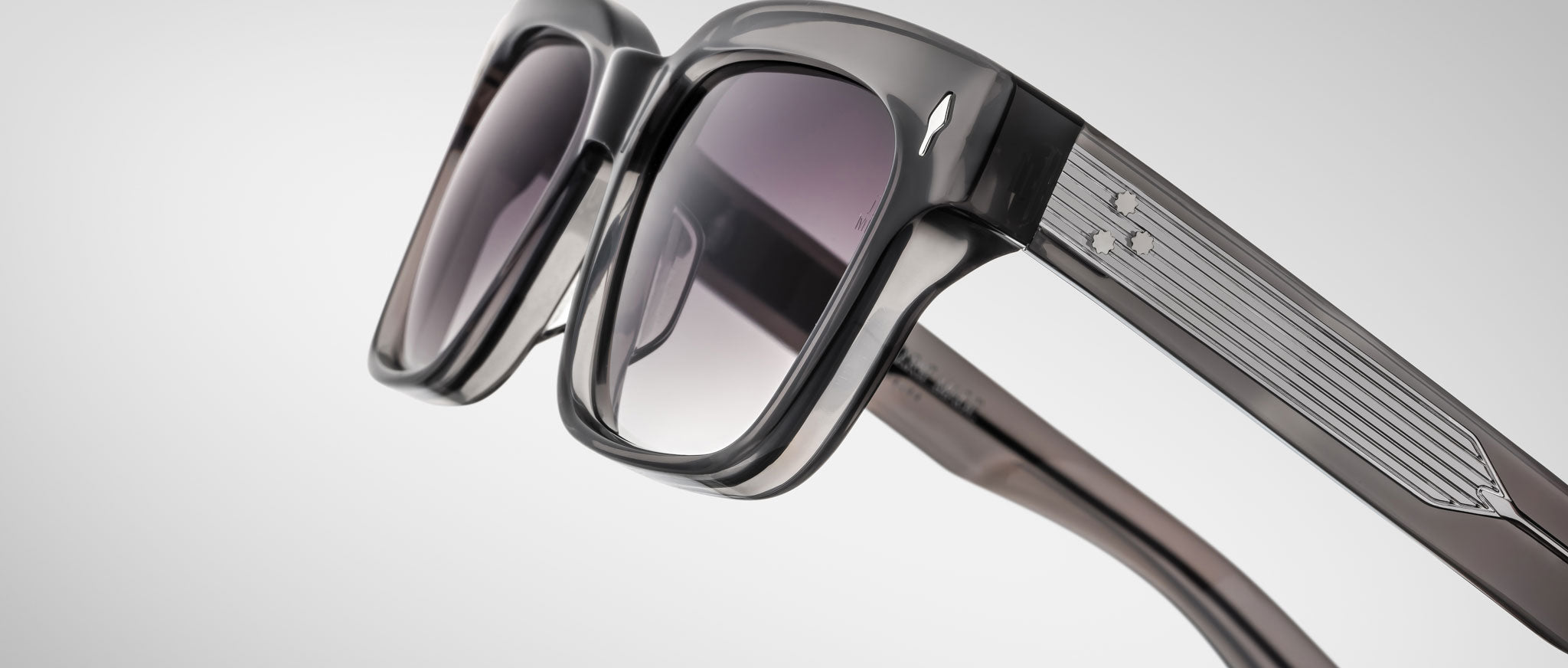 Close-up of Jacques Marie Mage Molino 55 sunglasses featuring stylish thick black frames, slightly tinted lenses, and metallic detailing on the arms against a light gray background.