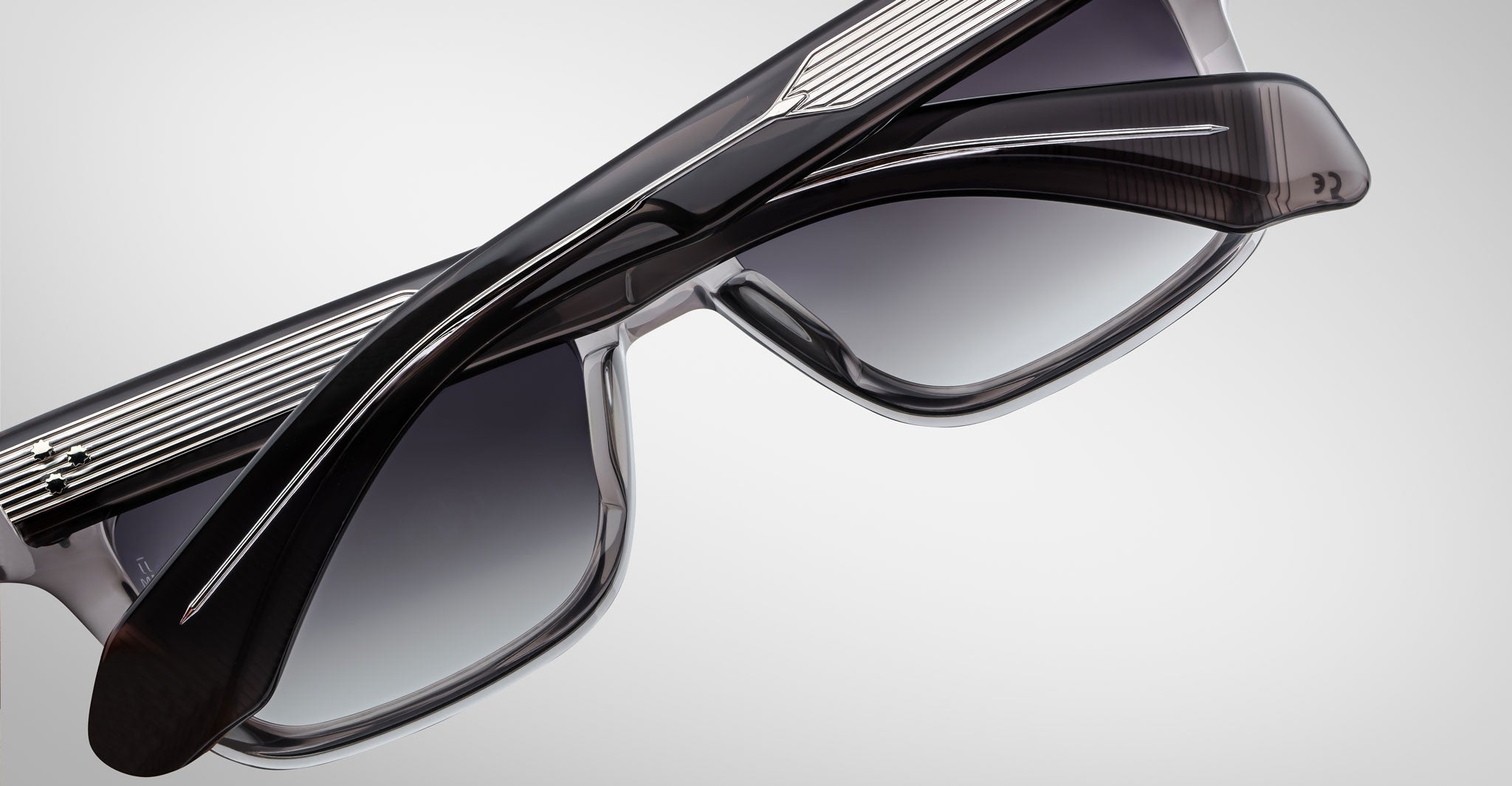 A close-up of two pairs of Jacques Marie Mage Molino 55 sunglasses with thick, dark frames and gradient lenses, overlapping each other against a light gray background.