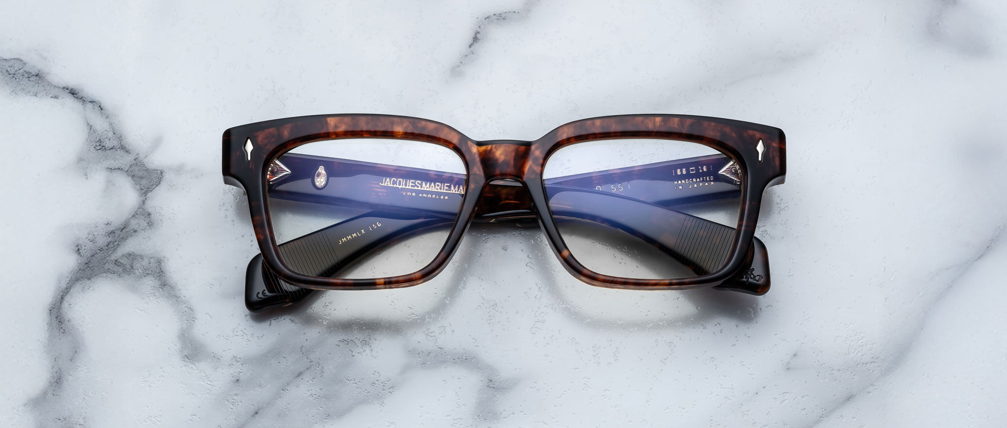 The Jacques Marie Mage Molino 55, a pair of rectangular tortoiseshell eyeglasses with clear lenses, rests on a white marble surface with gray veining.