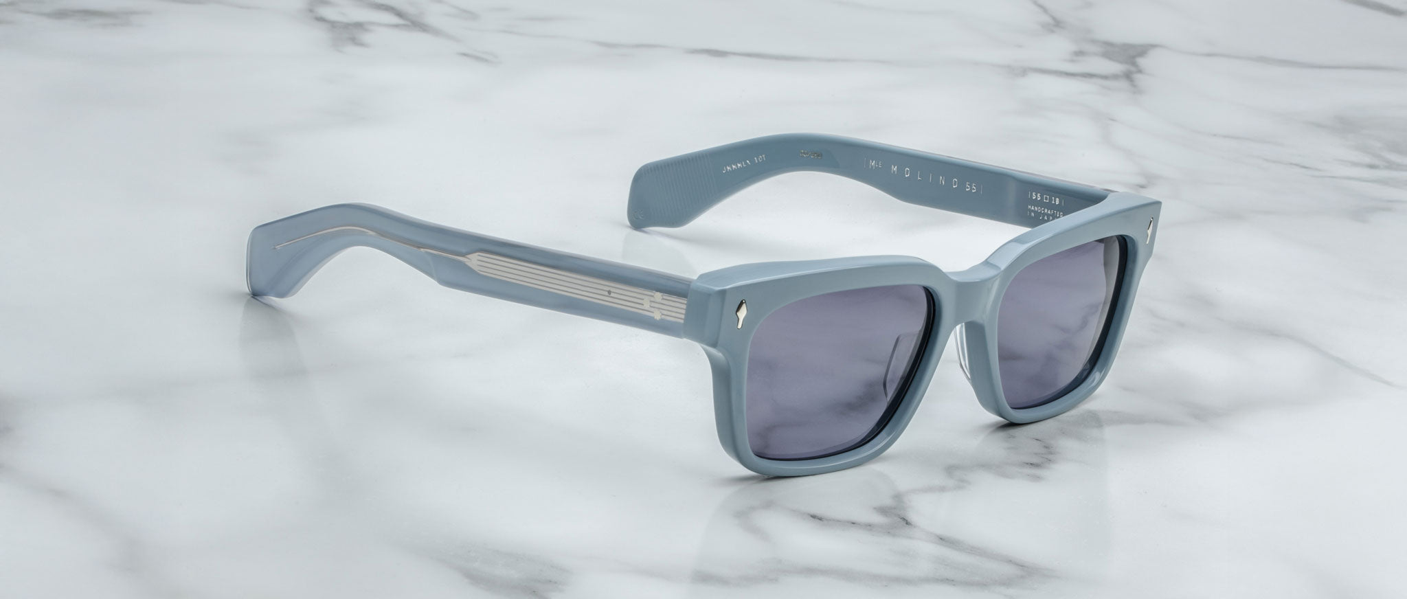 The Jacques Marie Mage Molino 55: light blue square sunglasses with dark lenses and thick frames are displayed on a white marble surface.