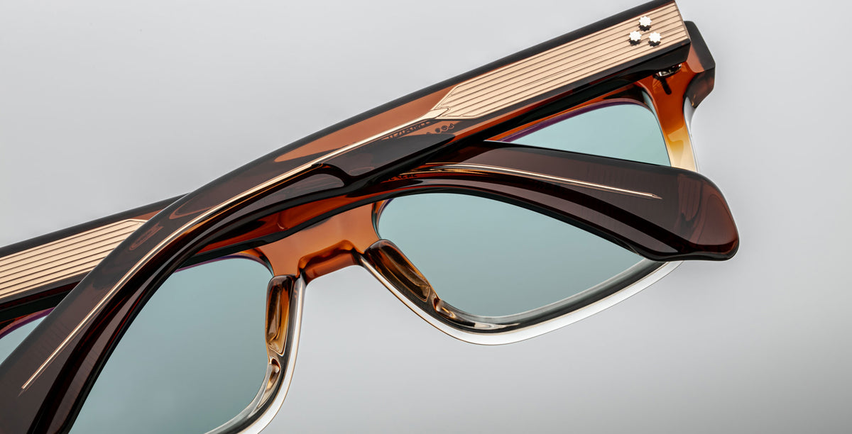 Close-up of two Jacques Marie Mage Molino eyeglasses, brown and gold frames, blue lenses, front view.