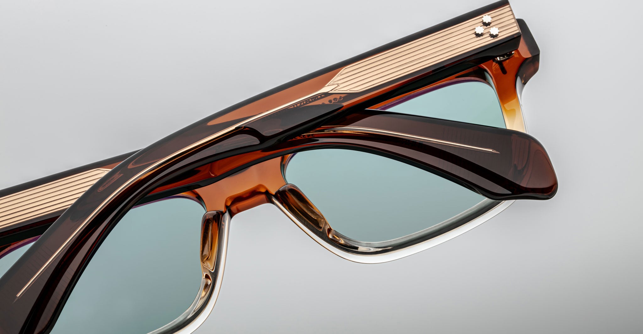 Close-up of two Jacques Marie Mage Molino eyeglasses, brown and gold frames, blue lenses, front view.