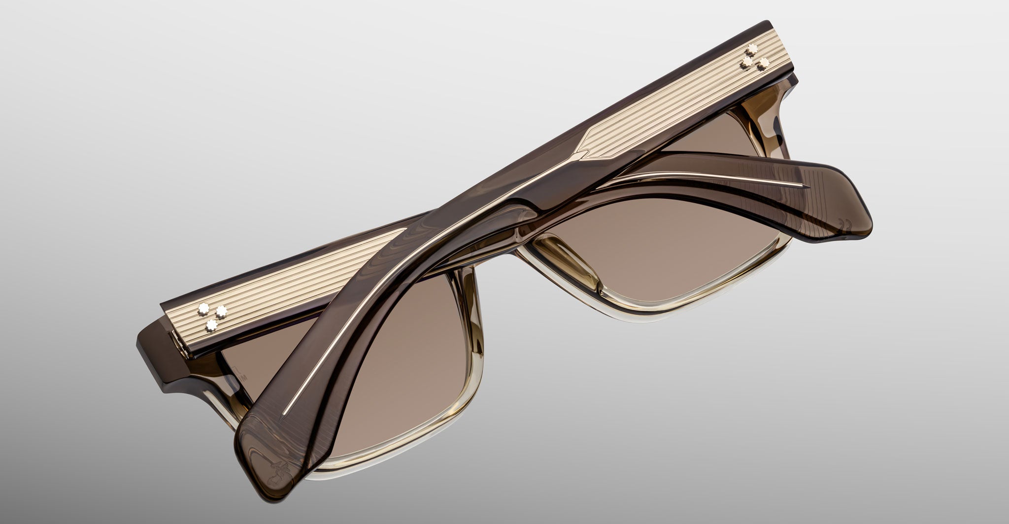The Jacques Marie Mage Molino by COMING SOON are stylish, square-shaped brown sunglasses with gold accents and ribbed temple detailing, shown folded on a light gray background.