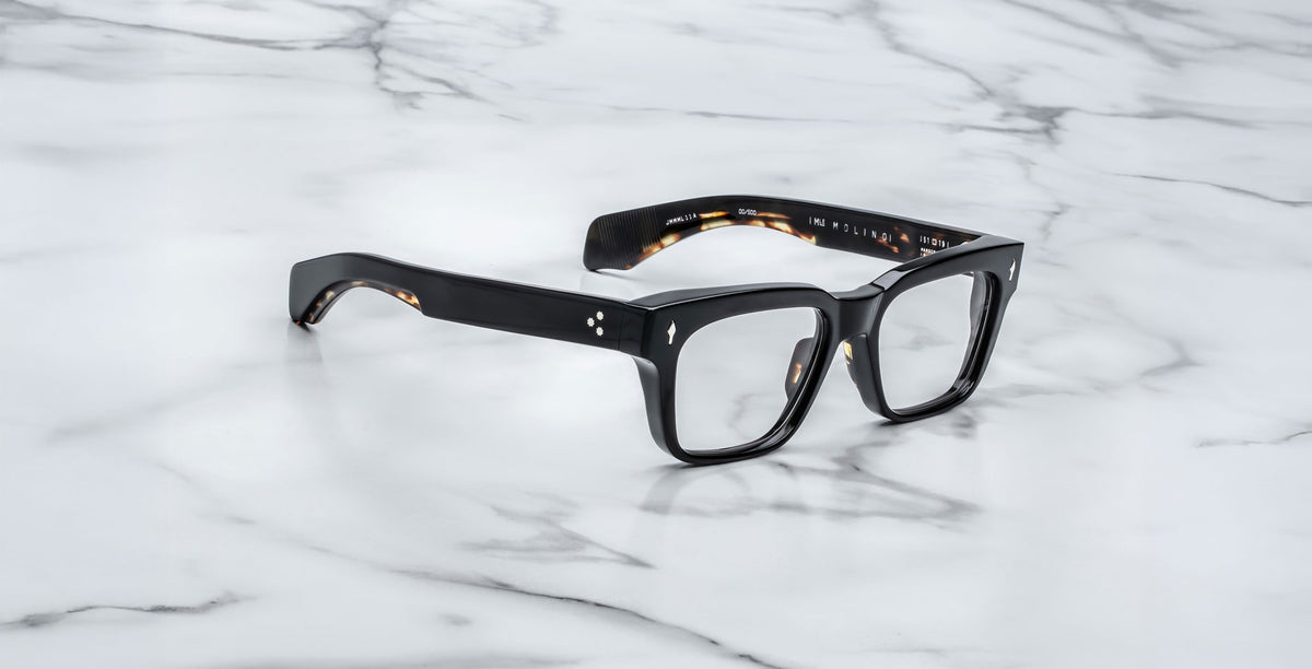 Jacques Marie Mage Molino black rectangular eyeglasses with thick frames displayed on a white marble surface with grey veining.