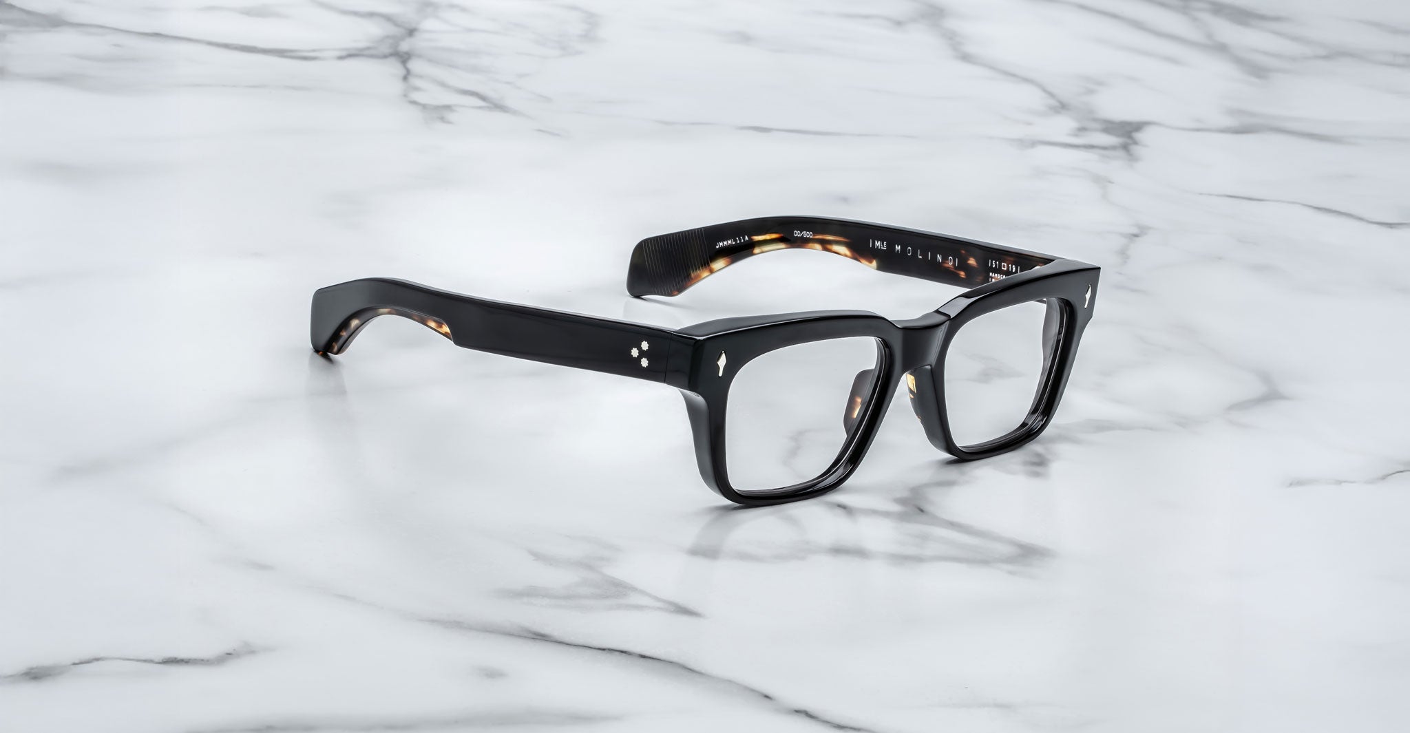Jacques Marie Mage Molino black rectangular eyeglasses with thick frames displayed on a white marble surface with grey veining.