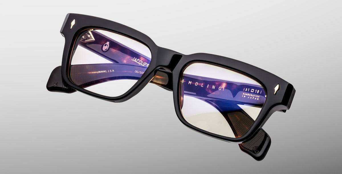 The Jacques Marie Mage Molino in Noir 15 features thick black rectangular frames, slightly tinted lenses, and visible brand markings on the temples, shown against a light gray background.
