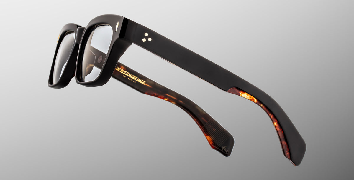 The Jacques Marie Mage Molino in Noir 15 black rectangular eyeglasses with thick frames and tortoiseshell-patterned inner arms, displayed on a light gray background.
