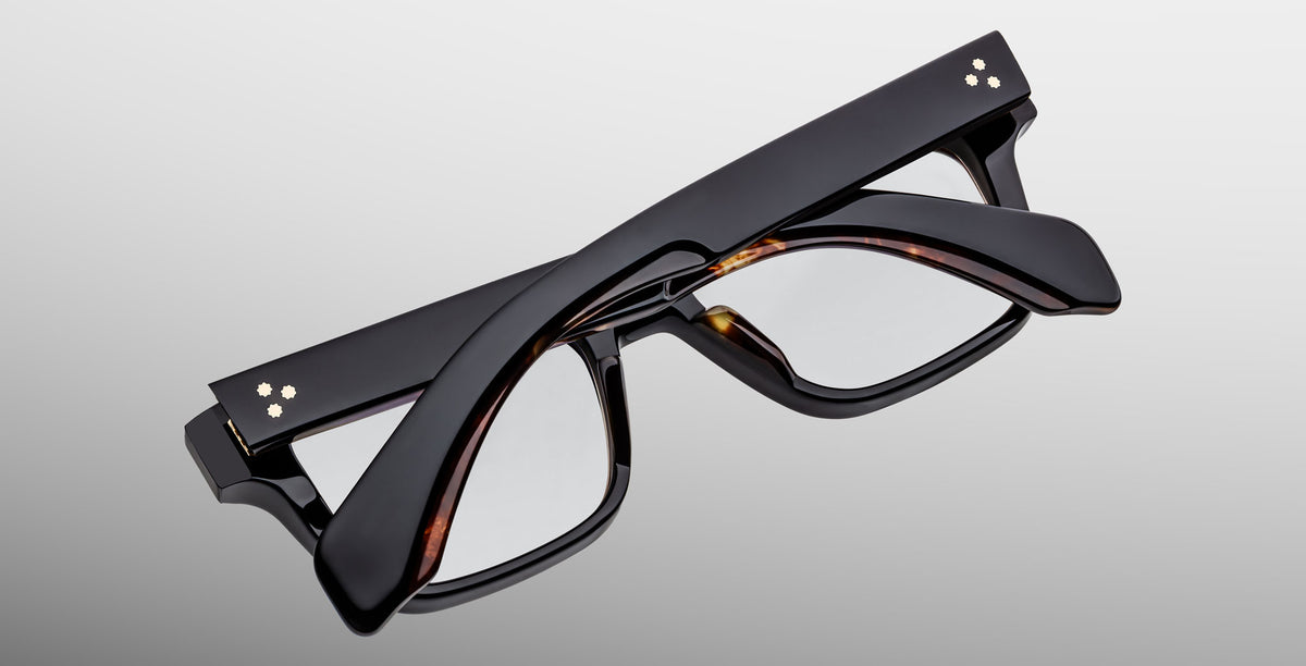 A pair of Jacques Marie Mage Molino black eyeglasses in Noir 15, folded flat with arms crossed, displayed on a plain light gray background.