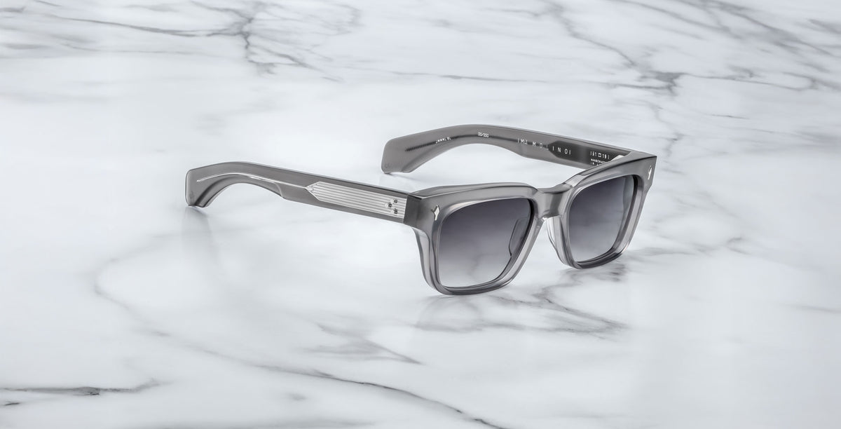 The Jacques Marie Mage Molino in Prime, featuring silver frames and dark lenses, rests on a white marble surface with gray veining.