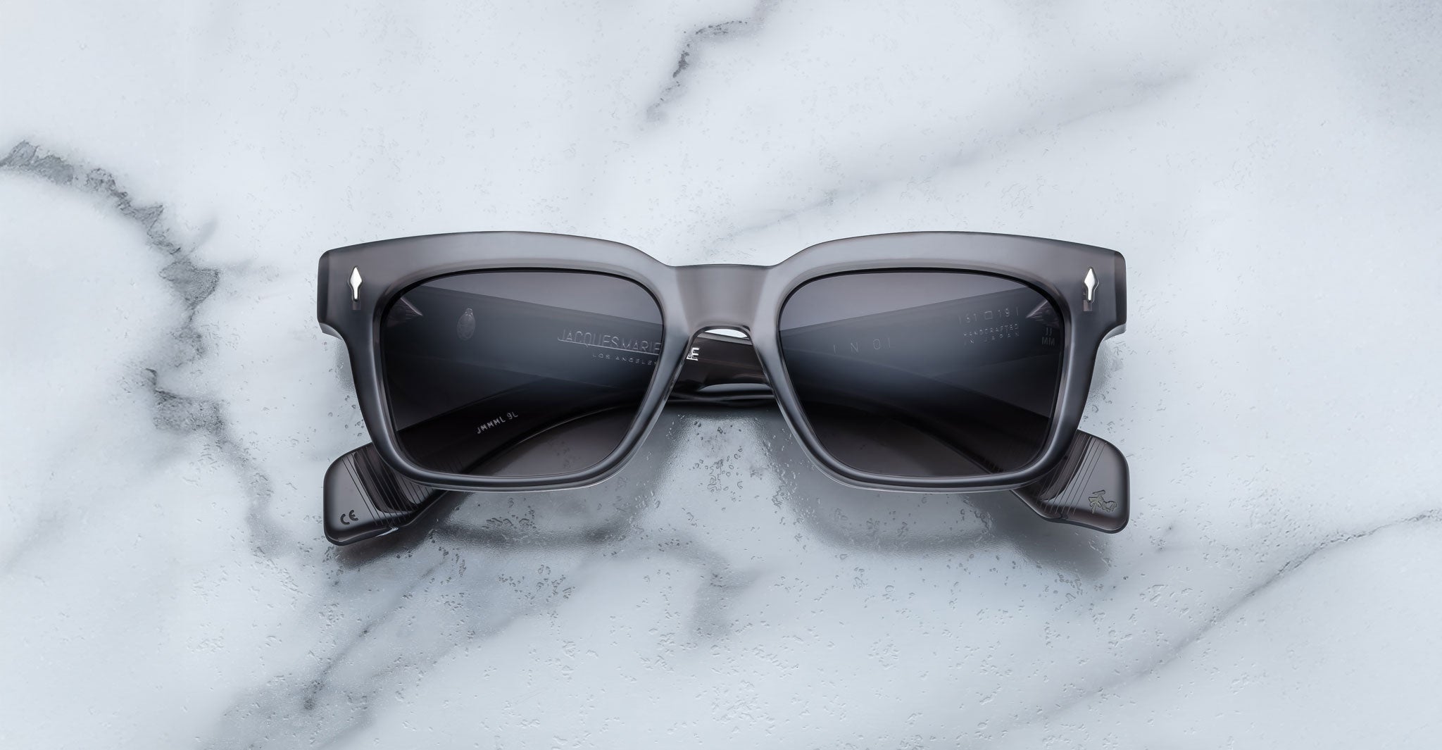 Jacques Marie Mage Molino rectangular gray sunglasses by COMING SOON, featuring dark tinted lenses, rest on a white marble surface.