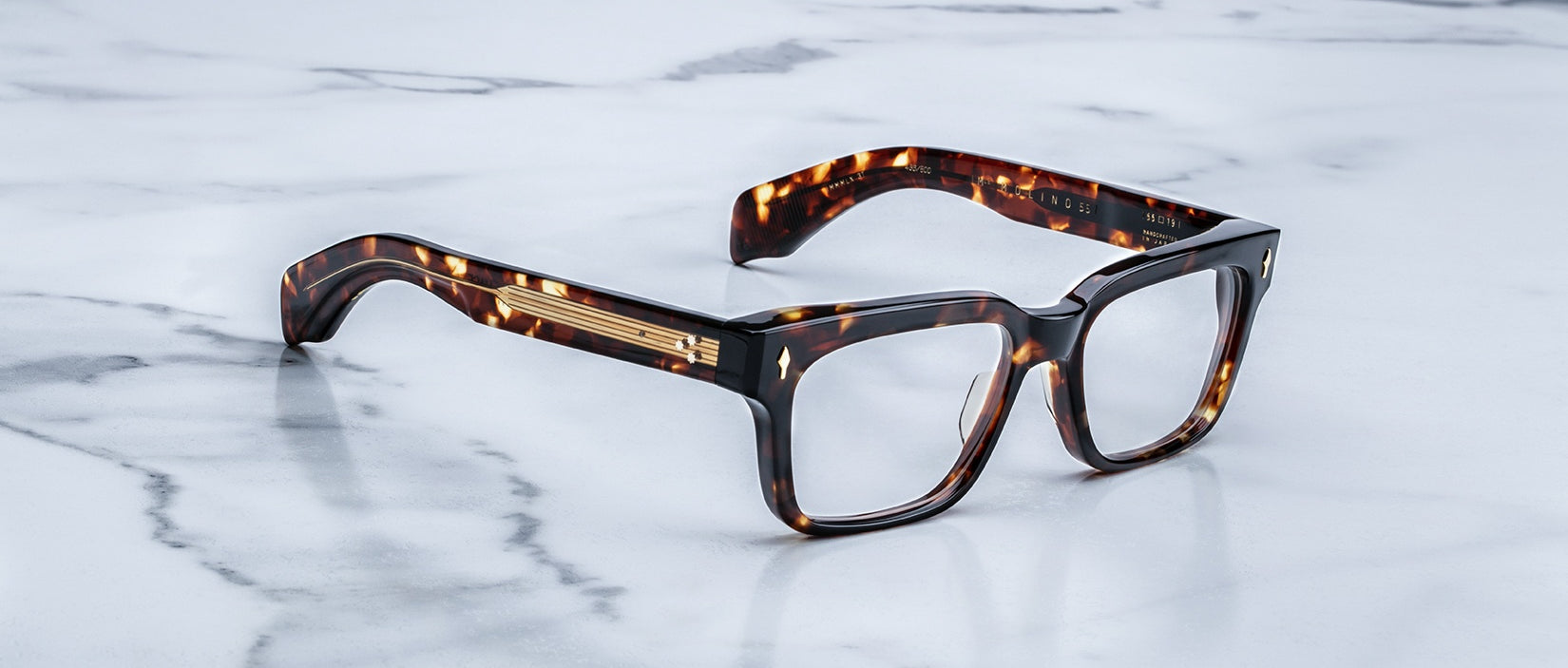 The Jacques Marie Mage Molino 55 tortoiseshell rectangular eyeglasses with thick frames rest on a white marble surface with grey veins.