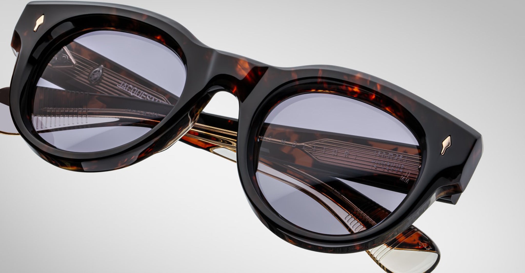 Close-up of Jacques Marie Mage Molitor sunglasses featuring stylish tortoiseshell frames, dark round lenses, and gold-accented arms, set against a light gray background.