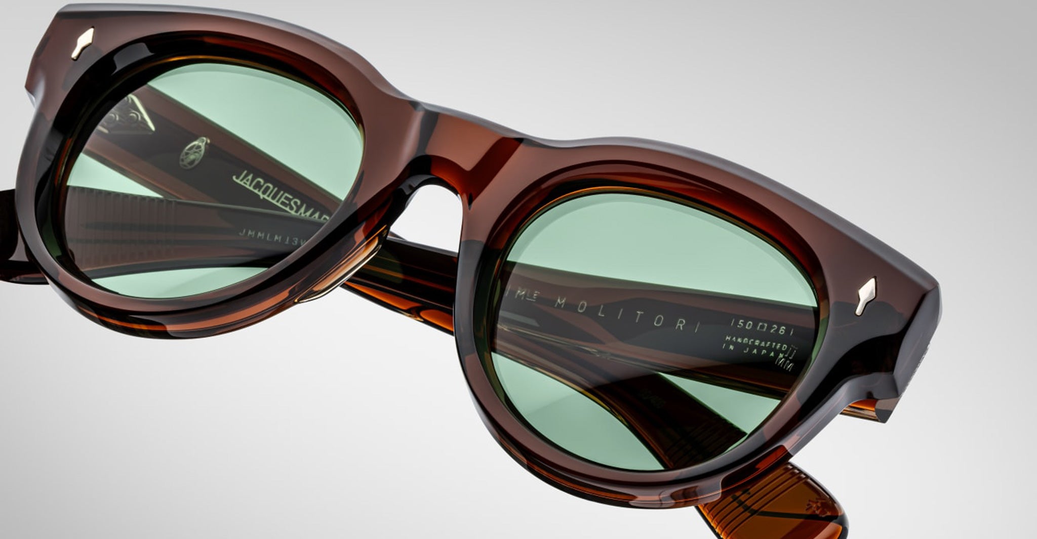 Close-up of Jacques Marie Mage Molitor sunglasses in brown acetate with green lenses, highlighting the frame details, engraved branding, and model info on the inner arms.