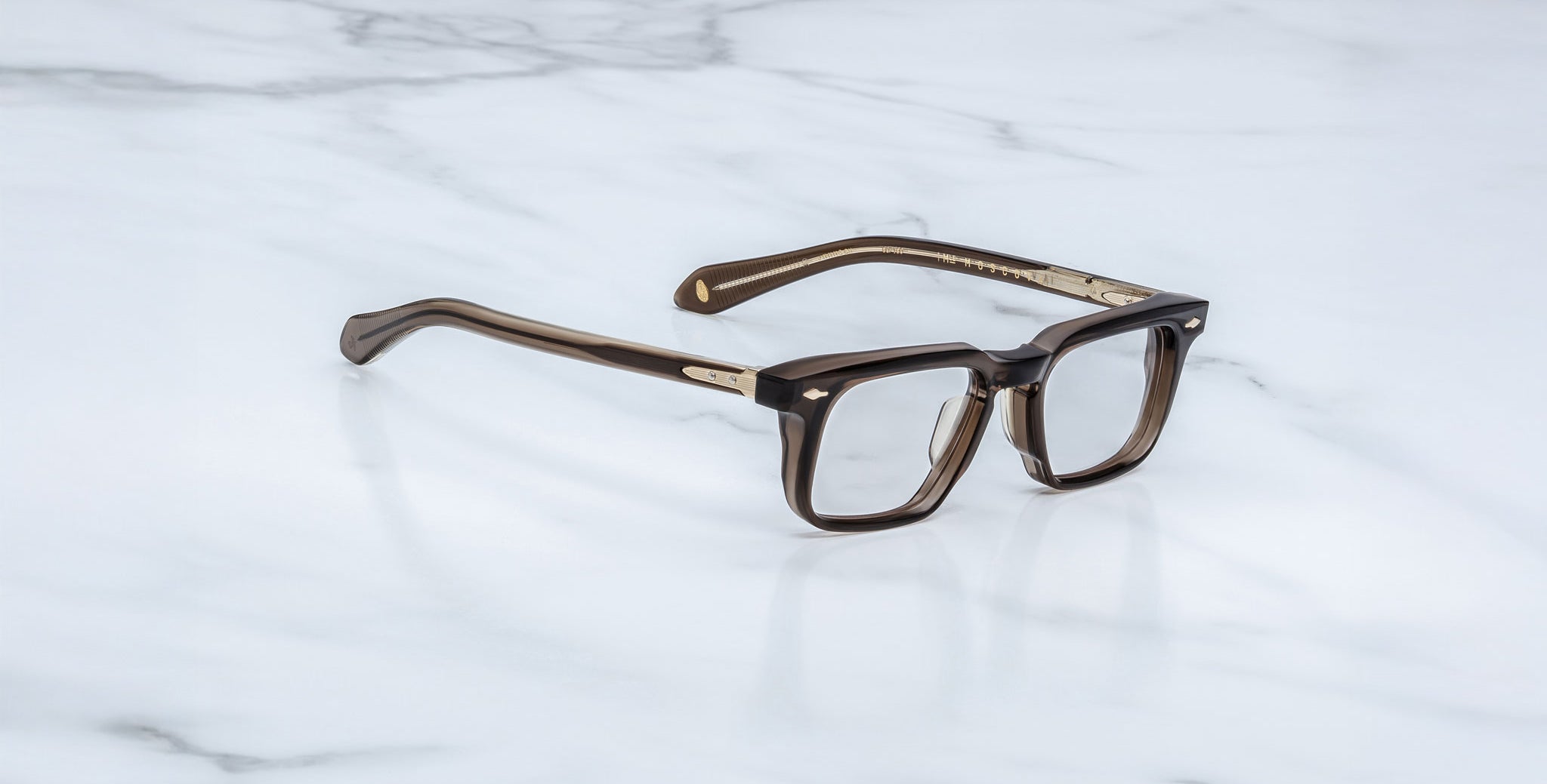 Jacques Marie Mage Moscova in London acetate optical frame, angled view with rectangular lenses, translucent brown acetate front, signature arrowhead pins, and exposed core wire temples with warm tonal detailing