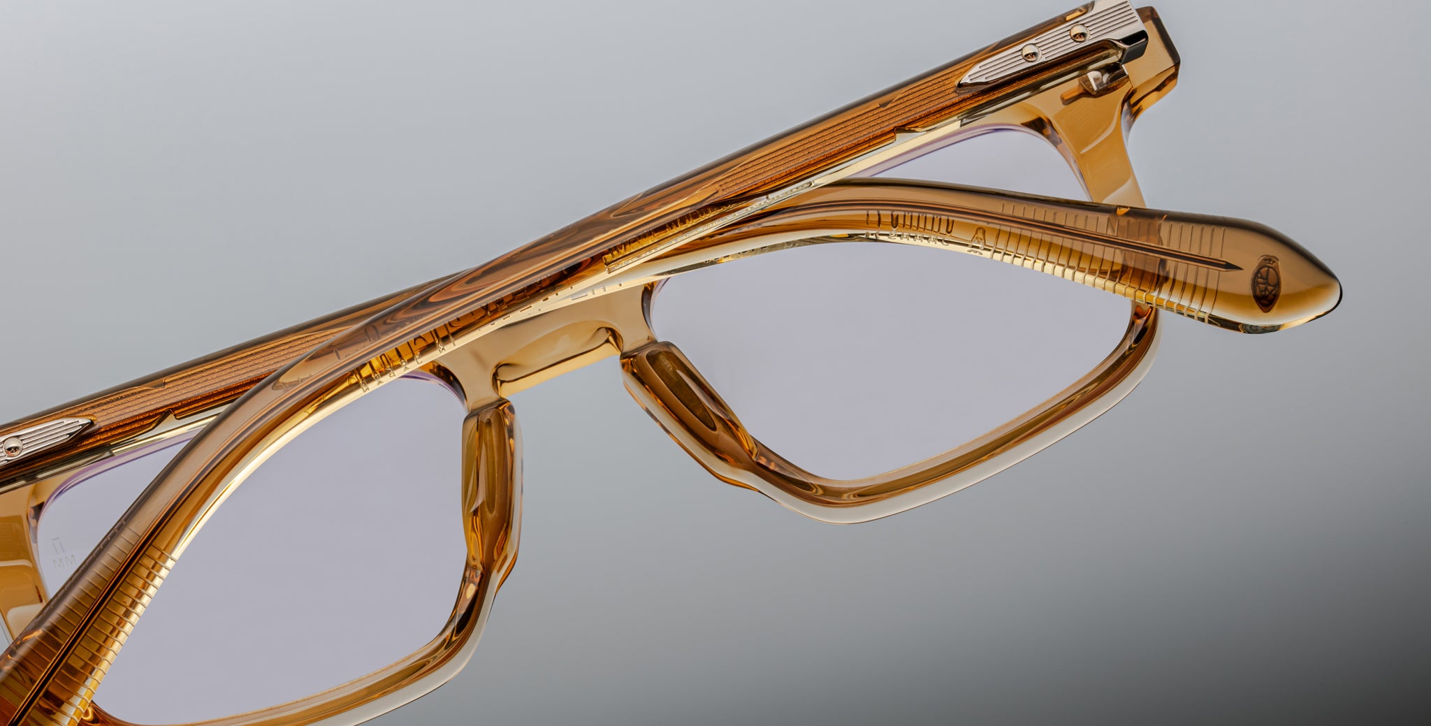 Close-up of Jacques Marie Mage Moscova eyeglasses, featuring translucent amber frames and clear lenses, with detailed texture and reflections on the frame set against a neutral gray background.