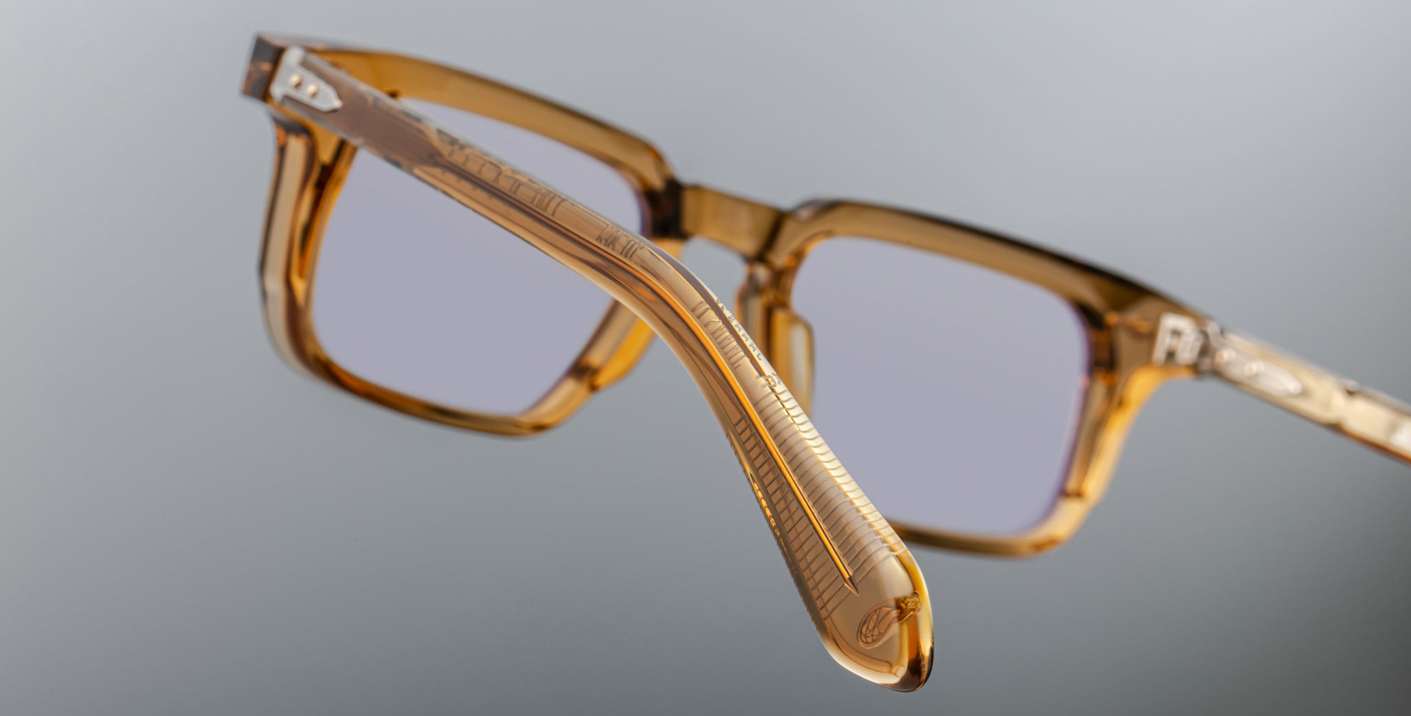 A close-up view of the side and front of the Jacques Marie Mage Moscova square translucent brown eyeglasses with clear lenses, displayed against a plain gray background.