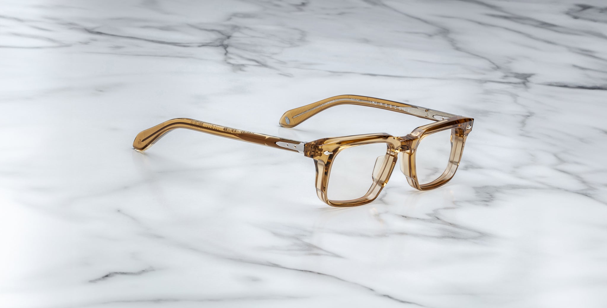 The Jacques Marie Mage Moscova brown transparent square-frame eyeglasses are displayed on a white marble surface with gray veining.