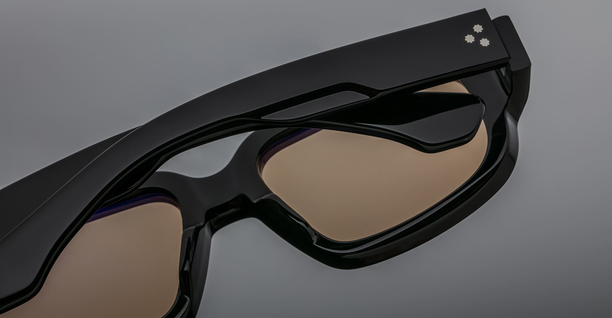 Close-up of Jacques Marie Mage Nakahira black smart glasses with tinted lenses, highlighting the right arm’s three small white indicator lights near the hinge, set against a neutral gray background.