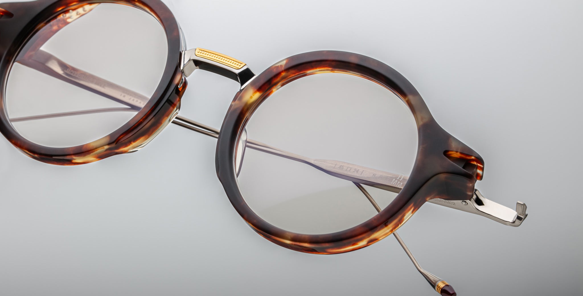 Close-up of Jacques Marie Mage Norman round eyeglasses in tortoiseshell with gold hinges and thin metal arms, frontal view.