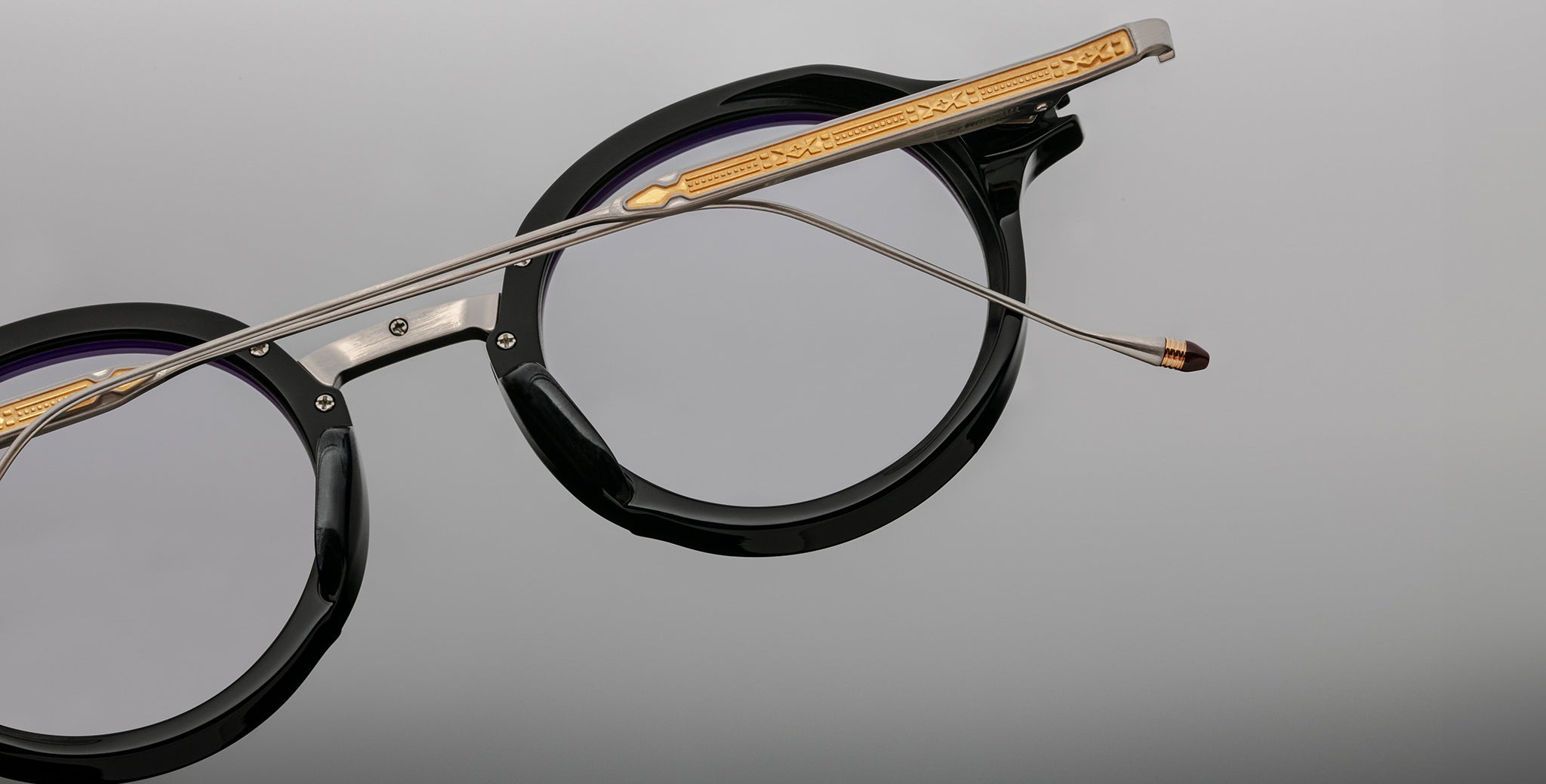Jacques Marie Mage Norman eyeglasses, black round frame with gold and silver arms, front view.