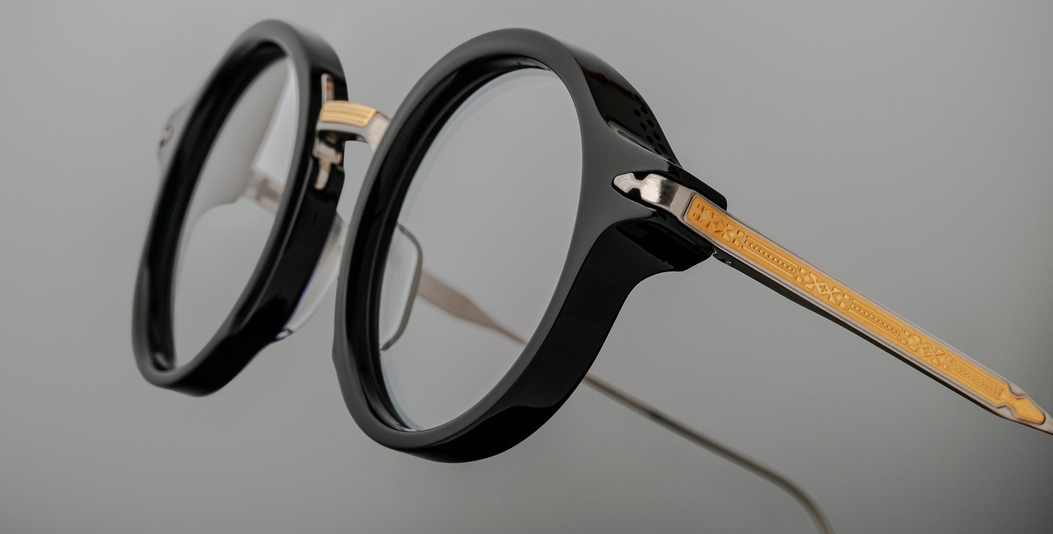 Close-up of Jacques Marie Mage Norman round black eyeglasses with gold patterned arms, showing front and side details.