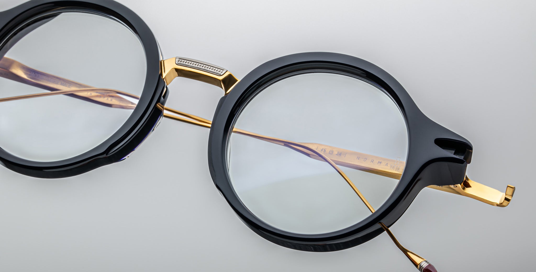 Jacques Marie Mage Norman round eyeglasses, black and gold frames, clear lenses, front view.