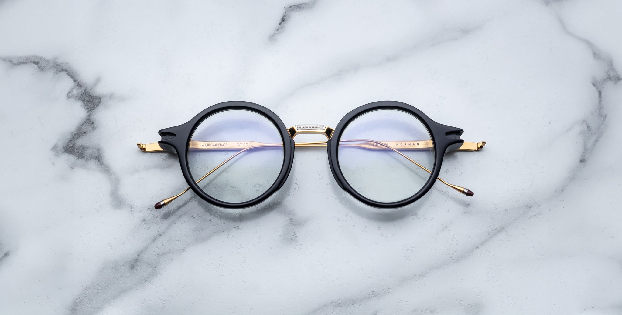 Jacques Marie Mage Norman round black eyeglasses with gold arms, top-down view.