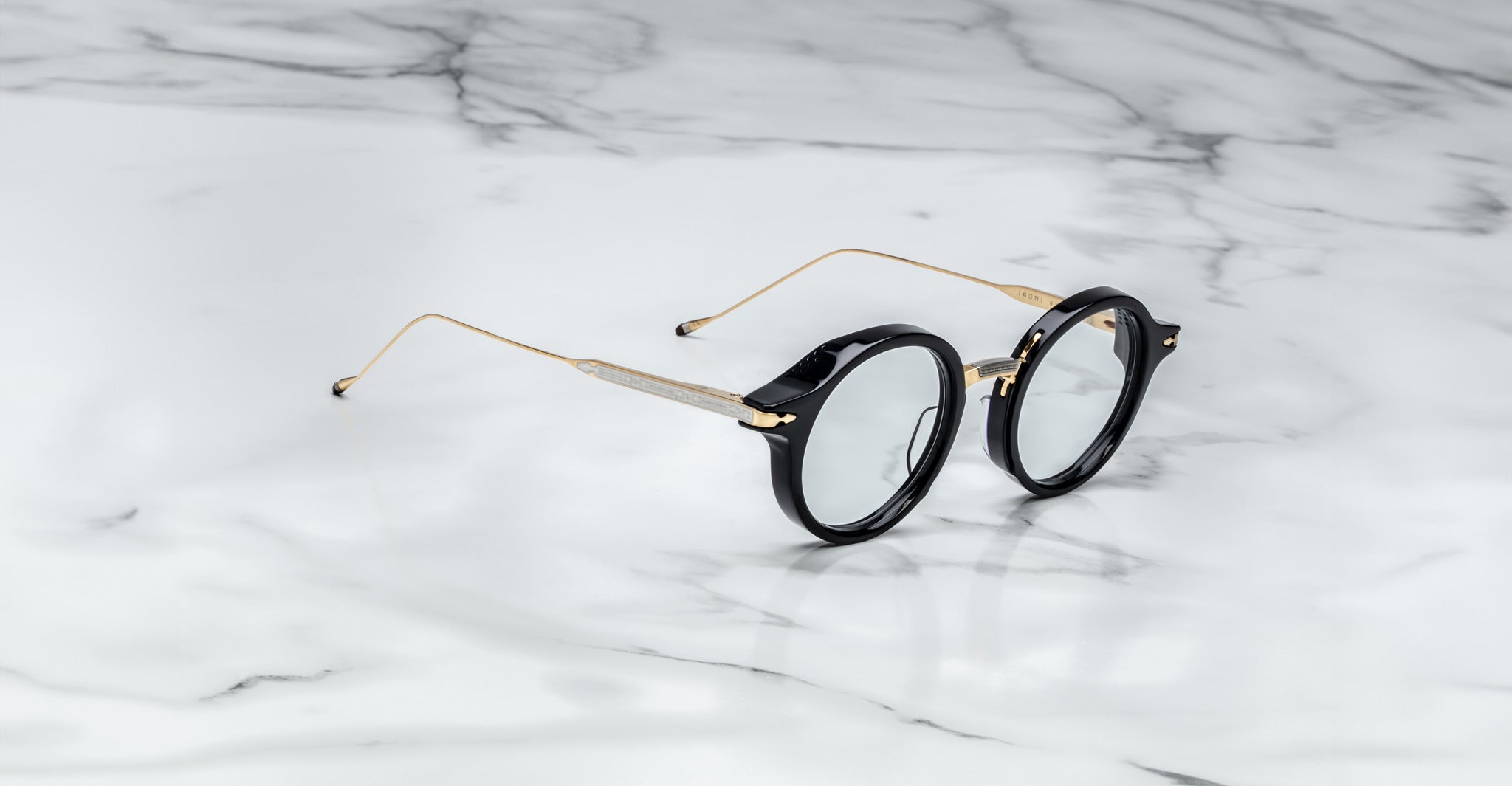 Jacques Marie Mage Norman eyeglasses with round black frames and gold temples, shown from the front.