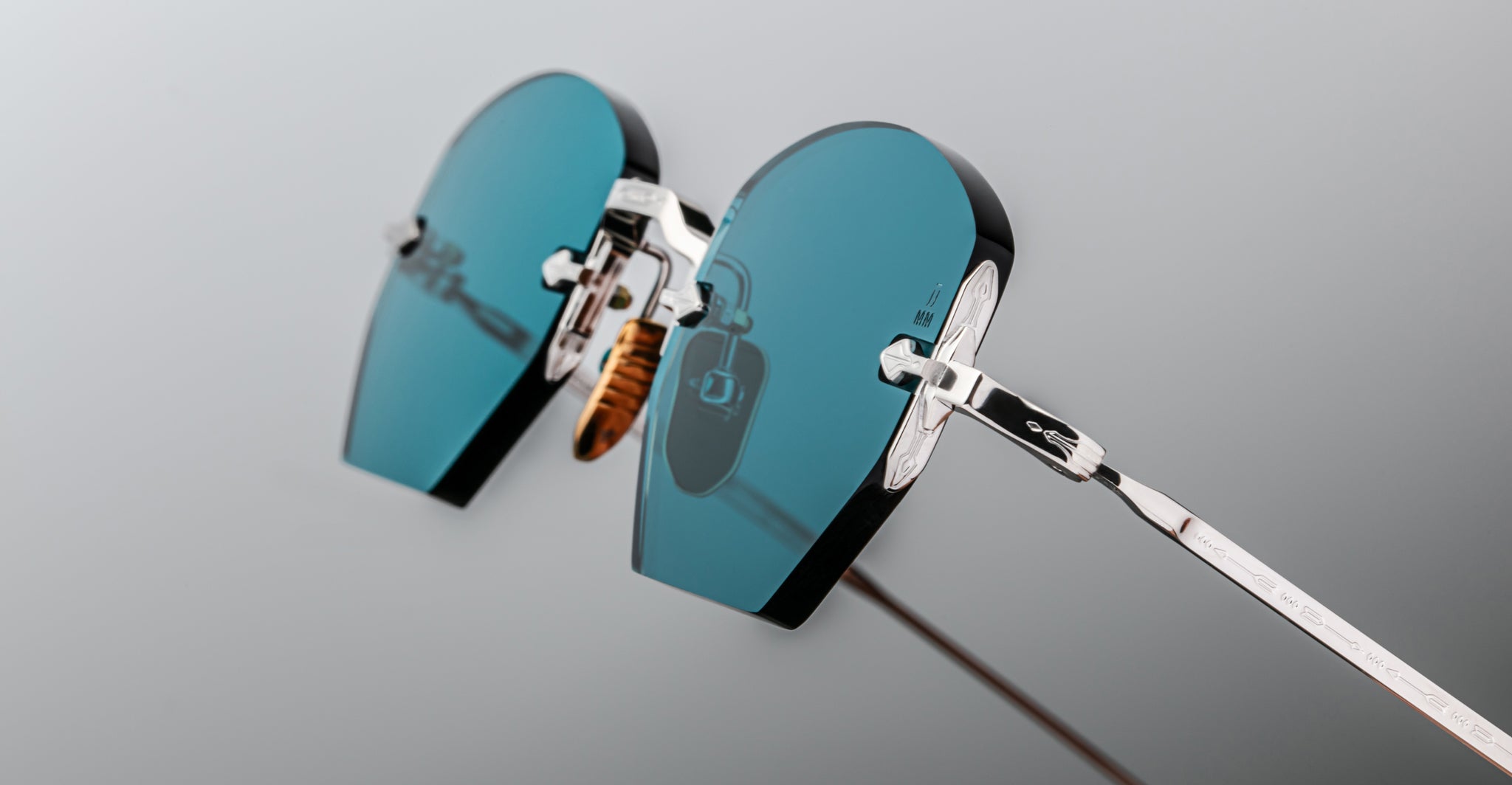 Close-up of Jacques Marie Mage Oatman by Jacques Marie Mage, featuring heart-shaped, teal-tinted lenses and silver metal frames inspired by handmade Japanese eyewear, set against a neutral background.