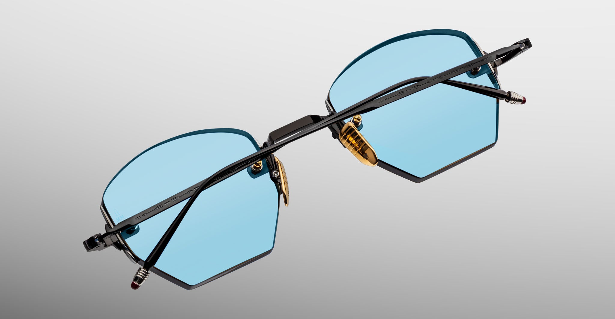 Jacques Marie Mage Oatman in Lagoon Blue eyeglasses feature hexagonal blue lenses, black frames, and gold nose pads, shown from a back angle.