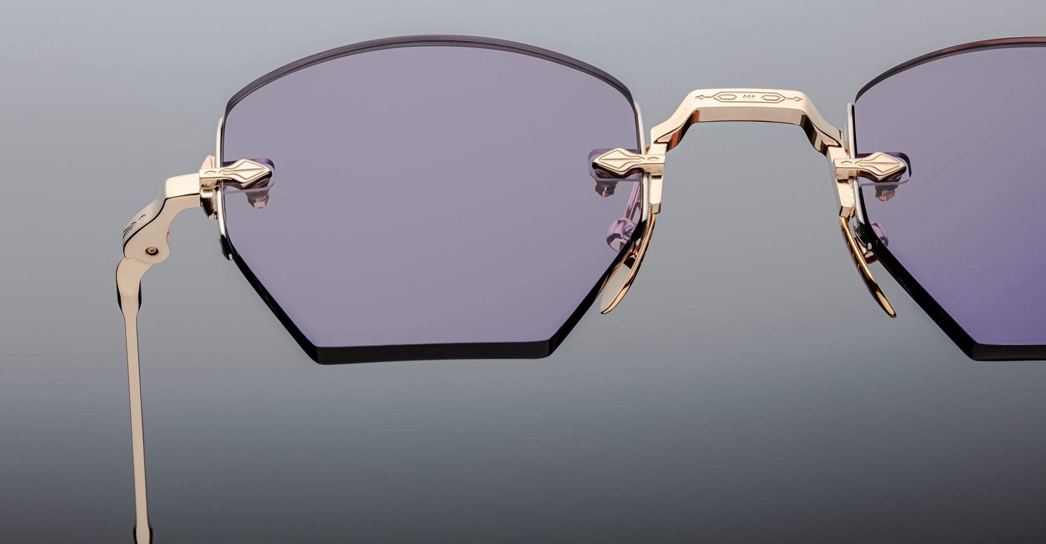 Close-up of Jacques Marie Mage Oatman hexagonal rimless sunglasses with gold metal frames and purple-tinted lenses, highlighting the craftsmanship of handmade Japanese eyewear by Jacques Marie Mage against a gradient background.