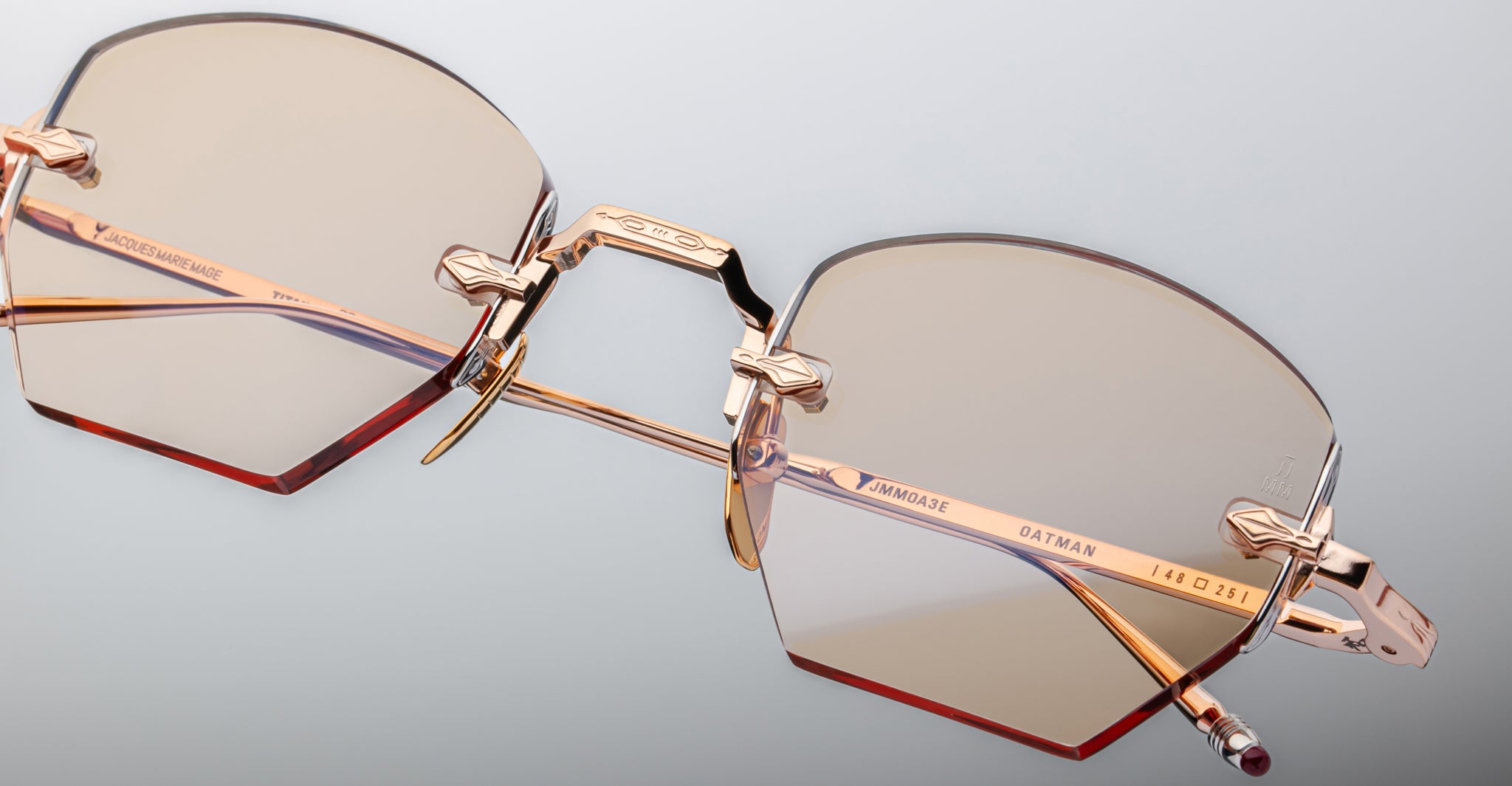 Close-up of Jacques Marie Mage Oatman hexagonal rimless sunglasses, with rose gold metal arms, light brown lenses, and detailed branding on the temples—showcasing exquisite handmade Japanese craftsmanship.