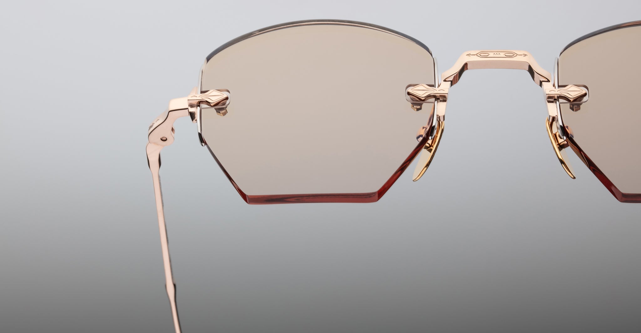 Close-up of the upper half of Jacques Marie Mage Oatman hexagonal rimless sunglasses, featuring gold metal frames and lightly tinted lenses, highlighting the refined elegance of Jacques Marie Mage against a light gray background.
