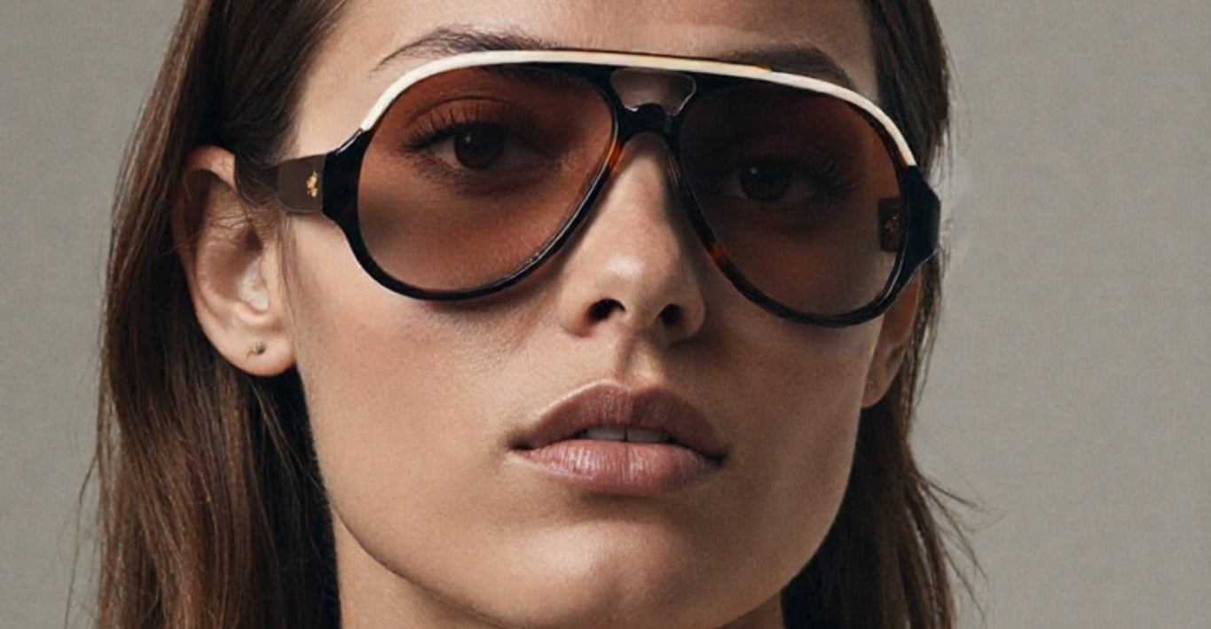Close-up of a model wearing Jacques Marie Mage Orion sunglasses in Havana, with a bold, oversized design in warm brown tones and gold accents, styled with a beige shirt and delicate jewelry